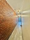 Corridor featuring brick wall, light wood-style floors, and a chandelier