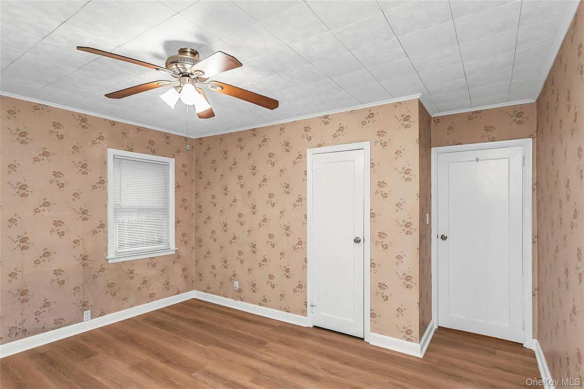 Room featuring wood-finish flooring, a ceiling fan with integrated lighting, and two white panel doors