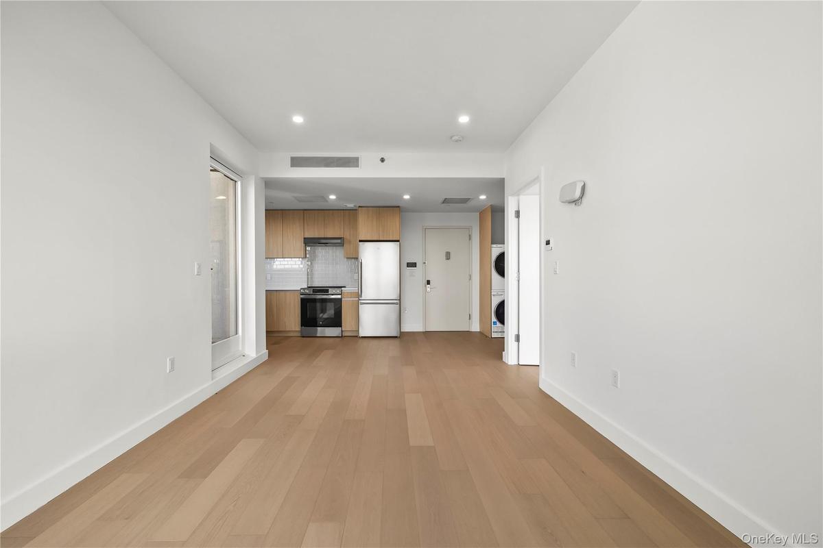 Unfurnished living room with light wood finished floors, stacked washer / dryer, and recessed lighting