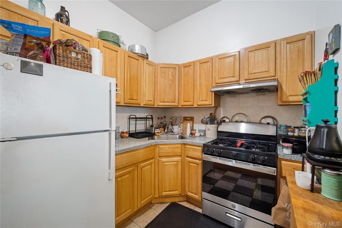Kitchen featuring a gas range with stainless steel accents, light wood-finish cabinetry, speckled countertops, and a tiled backsplash
