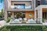 Elevated view of rear outdoor living terrace enclosed by glass railing, white woven lounge seating, wall-mounted TV on wood accent wall, stone façade