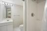 Bathroom featuring a white vanity with integrated sink, chrome faucet, white tile flooring, and a shower with a clear plastic curtain