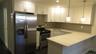 Contemporary kitchen featuring stainless steel appliances, white shaker cabinetry, a light-toned countertop, a subway tile backsplash, and dark wood-f