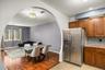 Kitchen and dining area featuring an arched doorway, wood-finish flooring, stainless steel refrigerator, wood cabinetry, and a mosaic tile backsplash