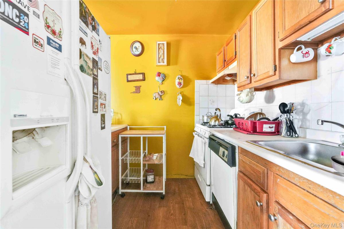 Kitchen with white appliances, light countertops, backsplash, dark wood-style floors, and under cabinet range hood