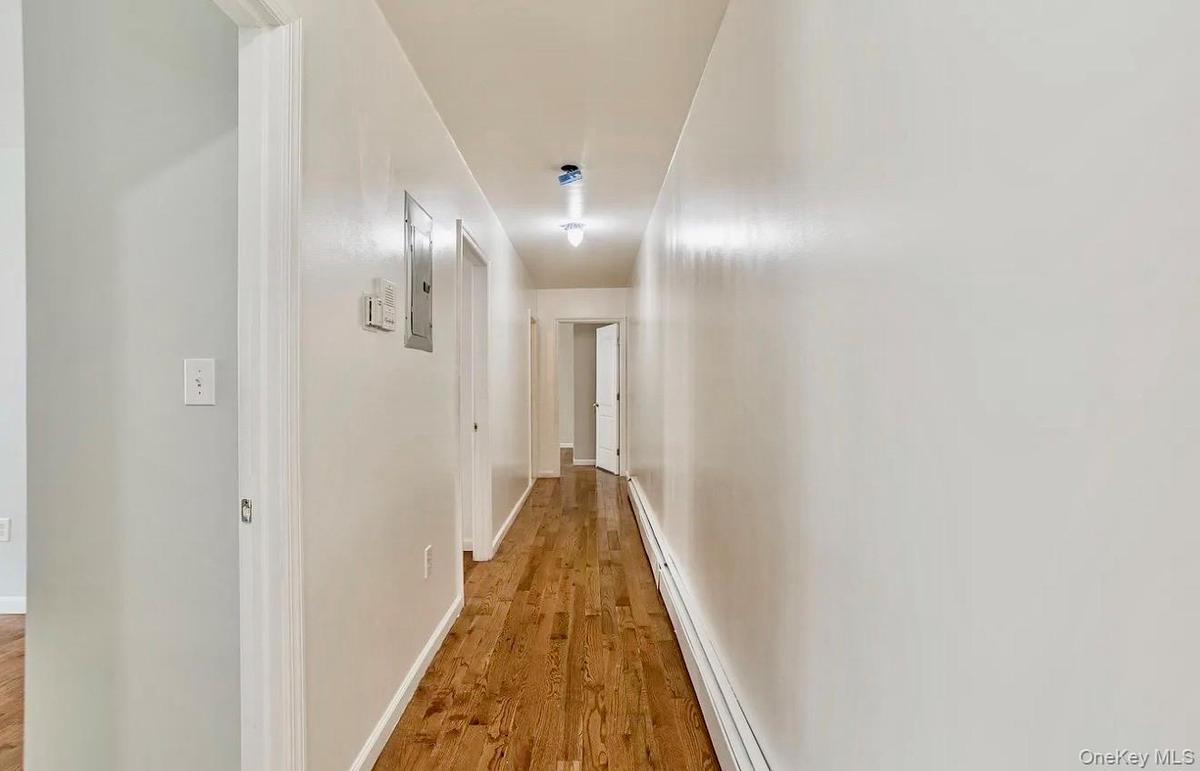 Hallway featuring wood-finish flooring, light-toned walls, and overhead lighting fixtures