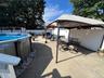 Expansive concrete patio with an above-ground pool, white privacy fencing, and mature perimeter trees