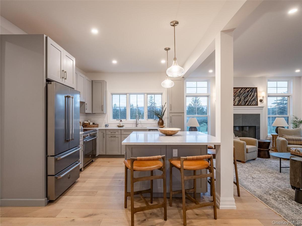 Kitchen with a tiled fireplace, high quality appliances, pendant lighting, light wood finished floors, and a kitchen breakfast bar