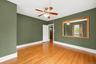 Spacious room featuring wood-finish flooring, a ceiling fan with integrated lighting, and a large wall-mounted mirror with a wood frame