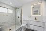 Bathroom en-suite featuring a frameless glass shower enclosure with gold-finish hardware, marble-look tiled walls, pebble shower pan, and a floating v