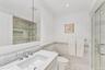 Full bathroom featuring crown molding, vanity, a marble finish shower, wainscoting, and tile walls.