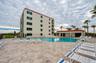 The resort-style pool includes a spacious deck, poolside lounge chairs, and a nearby clubhouse building, all set against a backdrop of palm trees and