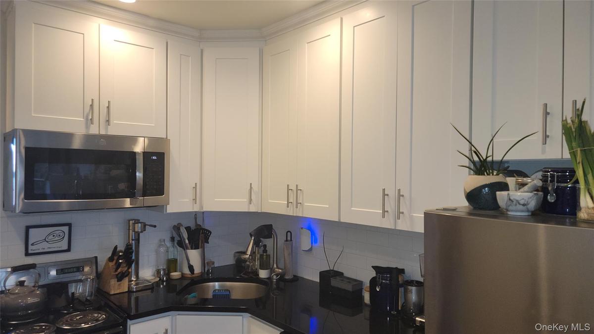 Kitchen featuring white cabinets, appliances with stainless steel finishes, decorative backsplash, and dark stone counters