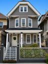 Gray siding exterior with white trim, a covered front porch supported by three columns, and a decorative wrought iron fence with a gate, and accompany
