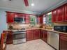 Kitchen with reddish brown cabinets, appliances with stainless steel finishes, light stone counters, decorative backsplash, and crown molding