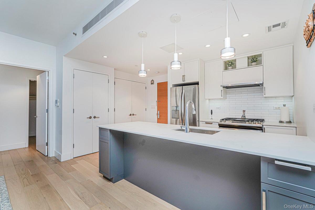 Kitchen featuring white cabinetry, decorative backsplash, pendant lighting, light wood-style flooring, and stainless steel appliances