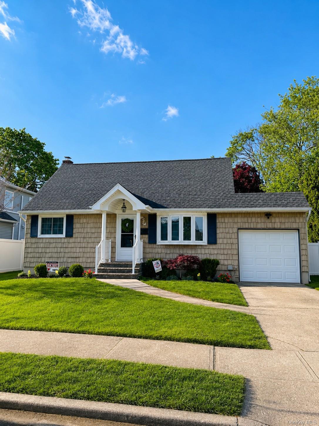 Shingle siding facade with dark blue shutters, covered entry with white railing, attached garage, paved driveway, and established front lawn