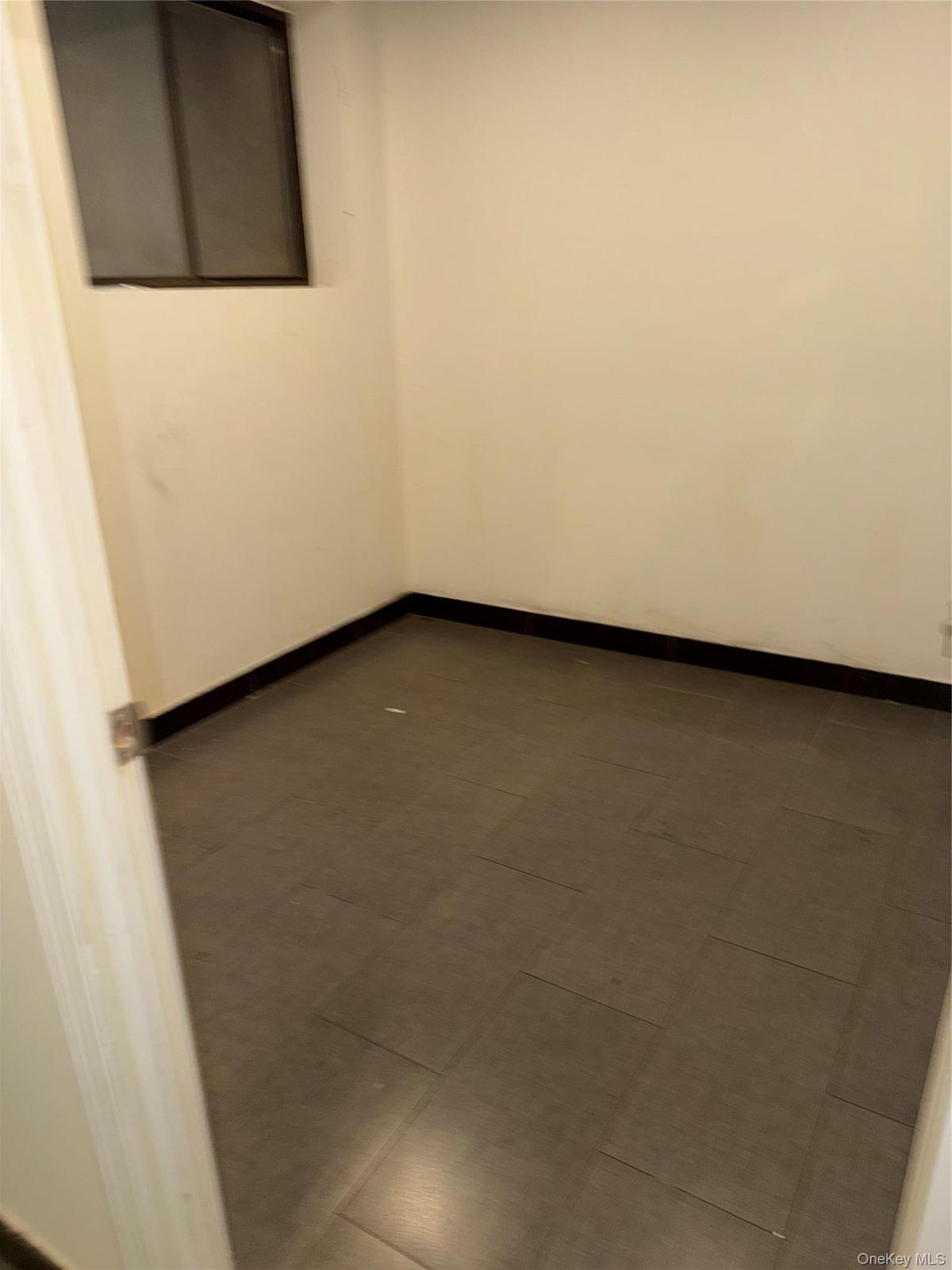 Compact room featuring light-colored walls, dark baseboards, and a window with a dark frame