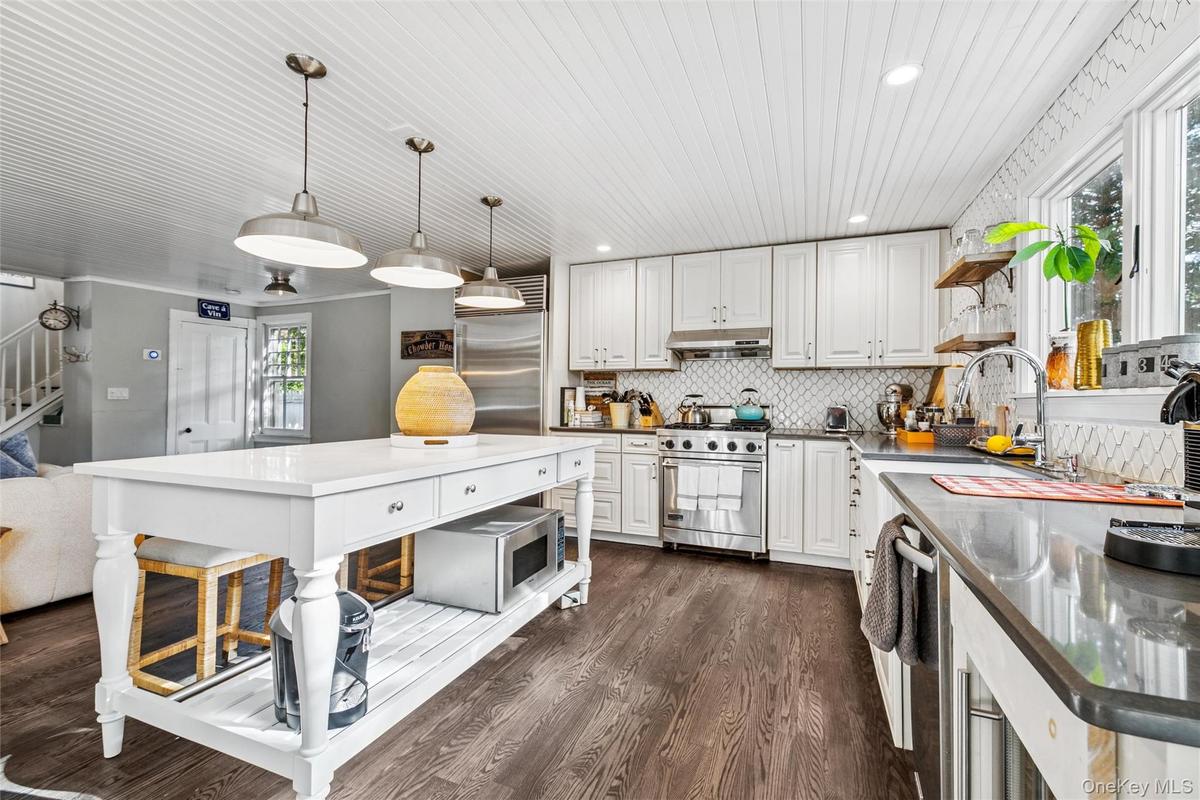Kitchen with open shelves, backsplash, dark wood-style floors, pendant lighting, and white cabinets