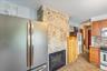 Kitchen with stainless steel appliances, a fireplace, light stone countertops, backsplash, and wood finish cabinetry