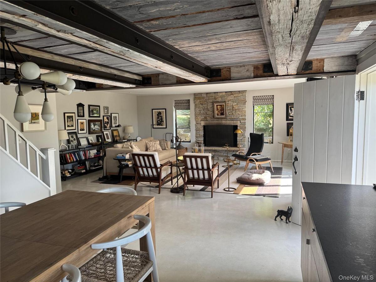 Dining space featuring stairs, a stone fireplace, finished concrete floors, and a wooden ceiling with exposed beams