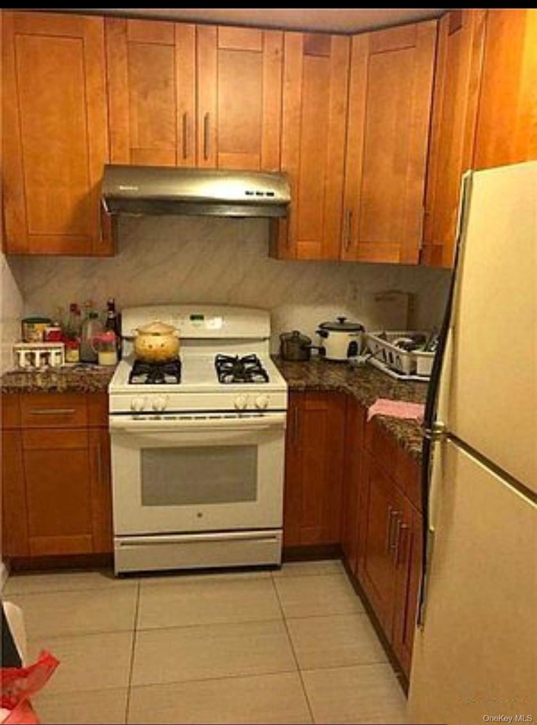 Kitchen featuring white appliances, light tile patterned flooring, brown cabinets, and under cabinet range hood