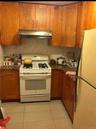 Kitchen featuring white appliances, light tile patterned flooring, brown cabinets, and under cabinet range hood