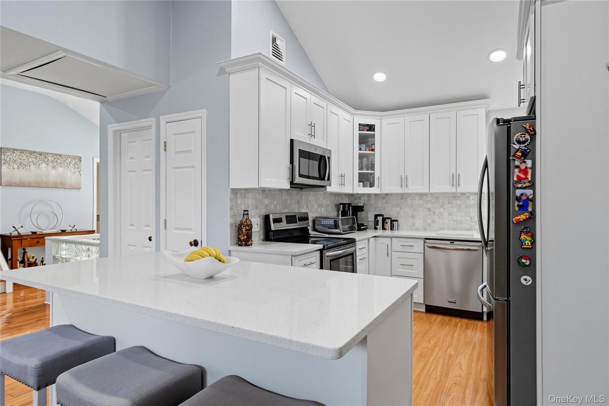 Kitchen featuring lofted ceiling, glass insert cabinets, stainless steel appliances, white cabinets, and light stone counters