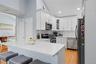 Kitchen featuring lofted ceiling, glass insert cabinets, stainless steel appliances, white cabinets, and light stone counters