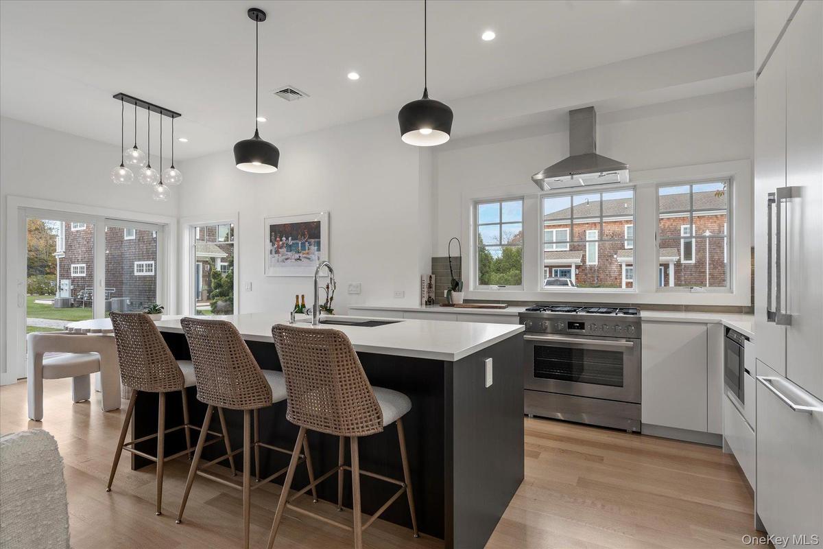 Kitchen featuring hanging light fixtures, appliances with stainless steel finishes, a breakfast bar, an island with sink, and extractor fan