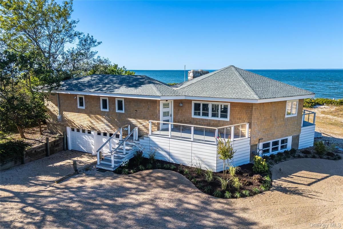 View of front of property featuring dirt driveway, roof with shingles, an attached garage, stairs, and a water view