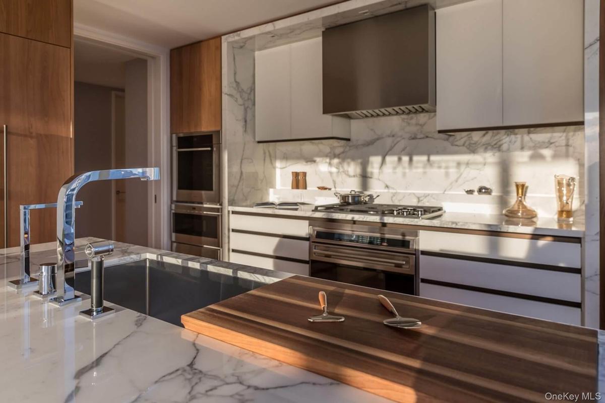 Kitchen featuring modern cabinets, wall chimney range hood, appliances with stainless steel finishes, backsplash, and a sink
