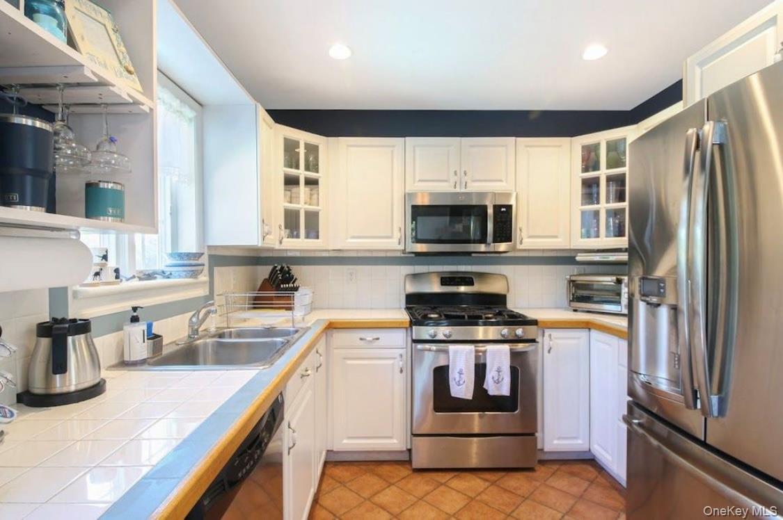 Kitchen featuring appliances with stainless steel finishes, white cabinets, glass insert cabinets, backsplash, and recessed lighting