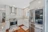 Kitchen with stainless steel appliances, wall chimney range hood, white cabinetry, dark wood-style floors, and light stone counters