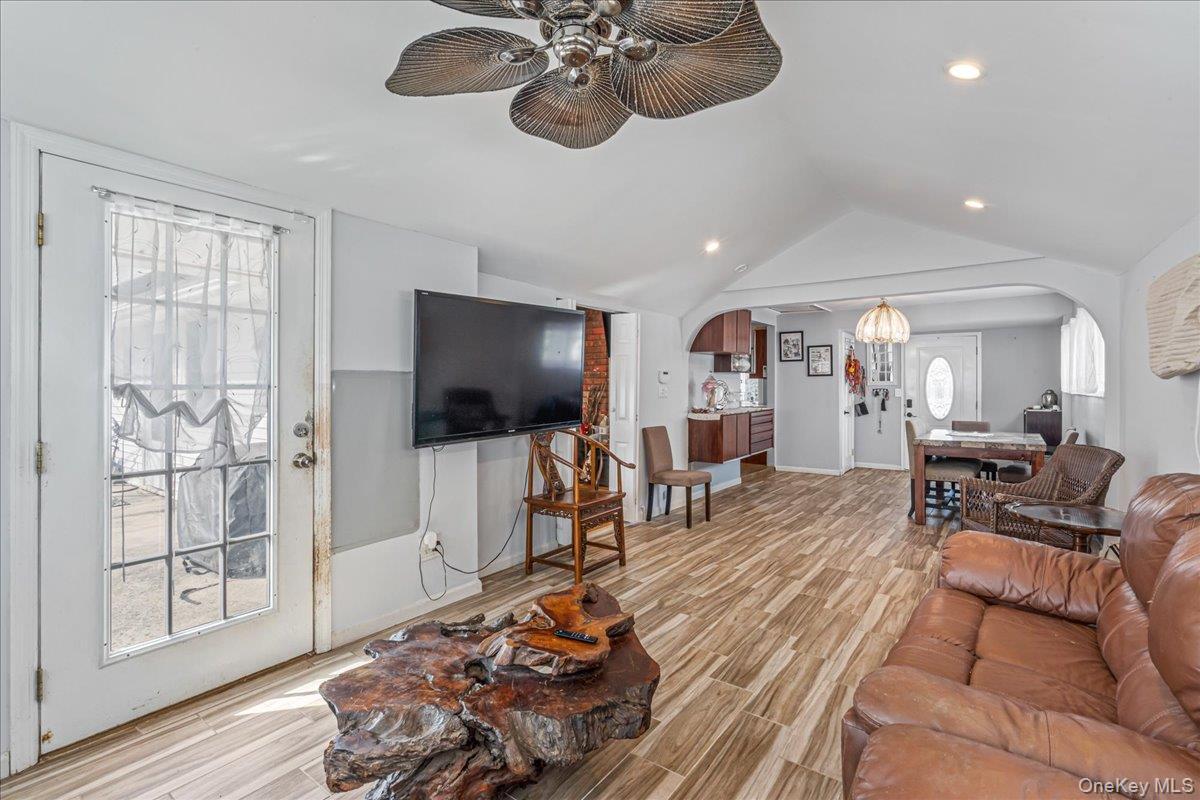 Living area with arched walkways, light wood-style floors, ceiling fan, and hanging lights