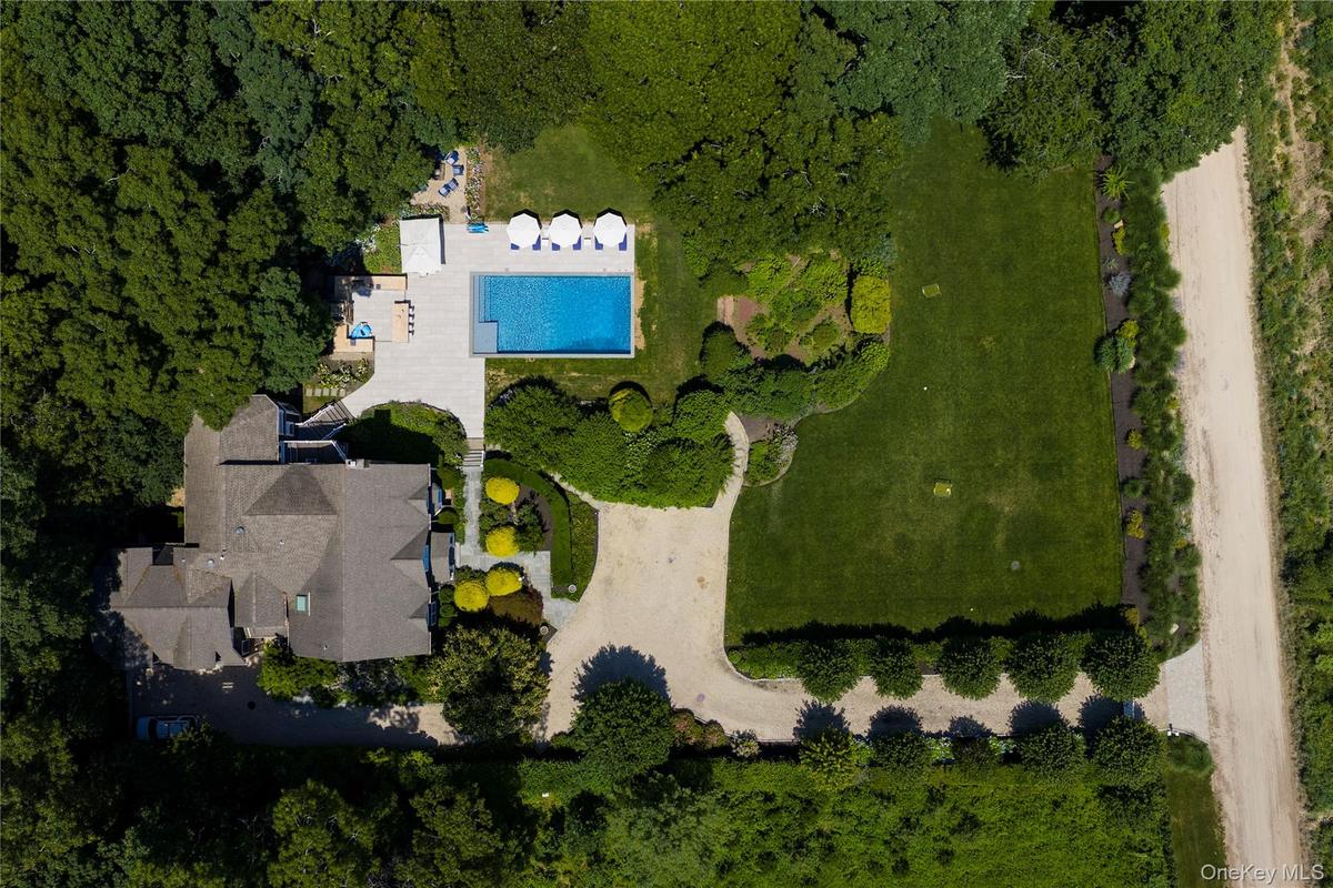 Expansive property featuring a large residence with a multi-gabled roofline, a rectangular swimming pool, and a gravel driveway