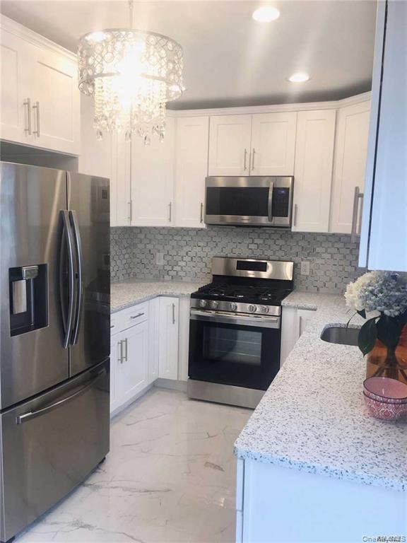Modern kitchen featuring white cabinetry, stainless steel appliances including a French-door refrigerator and gas range, quartz countertops, gray mosa