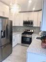 Modern kitchen featuring white cabinetry, stainless steel appliances including a French-door refrigerator and gas range, quartz countertops, gray mosa