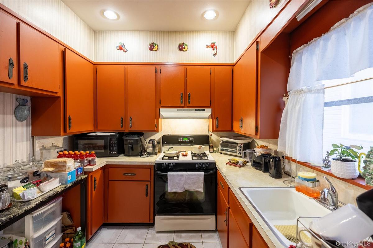 Kitchen with gas range oven, light tile patterned floors, light countertops, and black microwave