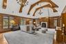 Grand family room featuring soaring vaulted ceilings with striking wood beams and rich paneled walls. A stately fireplace anchors the space, creating