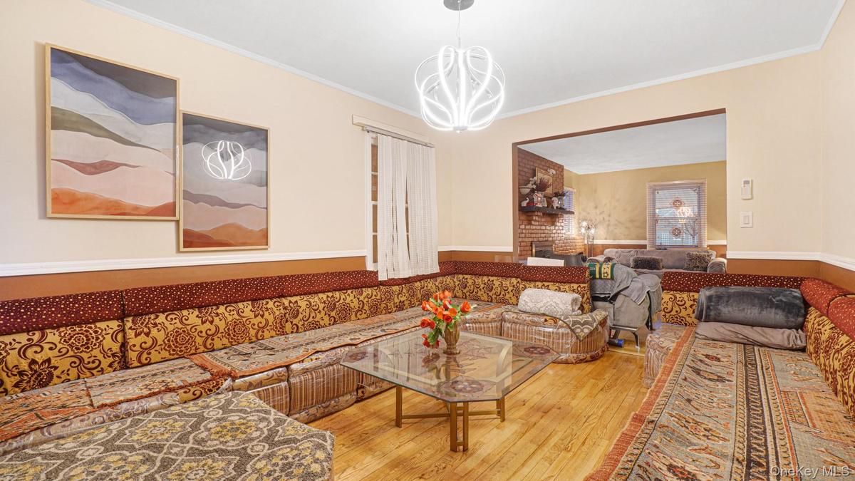 Living room with wood-type flooring, crown molding, a wainscoted wall, and a chandelier