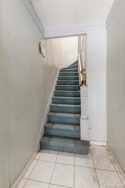 Stairs with tile patterned flooring and wood walls