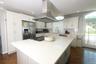 Spacious kitchen featuring an expansive center island, white cabinetry, a stainless steel refrigerator, a professional-grade range hood, and wood-fini