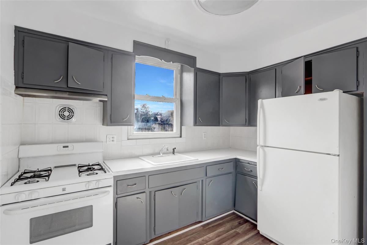 Kitchen with white appliances, gray cabinetry, light countertops, dark wood-style floors, and tasteful backsplash