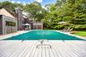 View of pool featuring a covered pool, outdoor dining space, view of wooded area, a deck, and a patio area