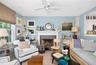 Living area featuring a white ceiling fan, light blue walls, and a fireplace with a white mantel and stone surround