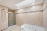 Bathroom featuring a built-in jetted tub, a glass-enclosed shower, a skylight, recessed lighting, and louvered bifold doors