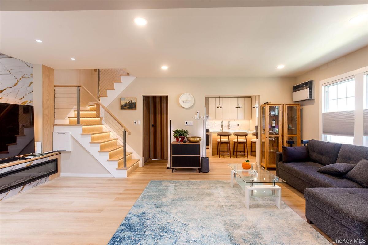 Open-concept living area featuring light wood-finish flooring, recessed ceiling lighting, a built-in linear fireplace with a marble-finish surround, a