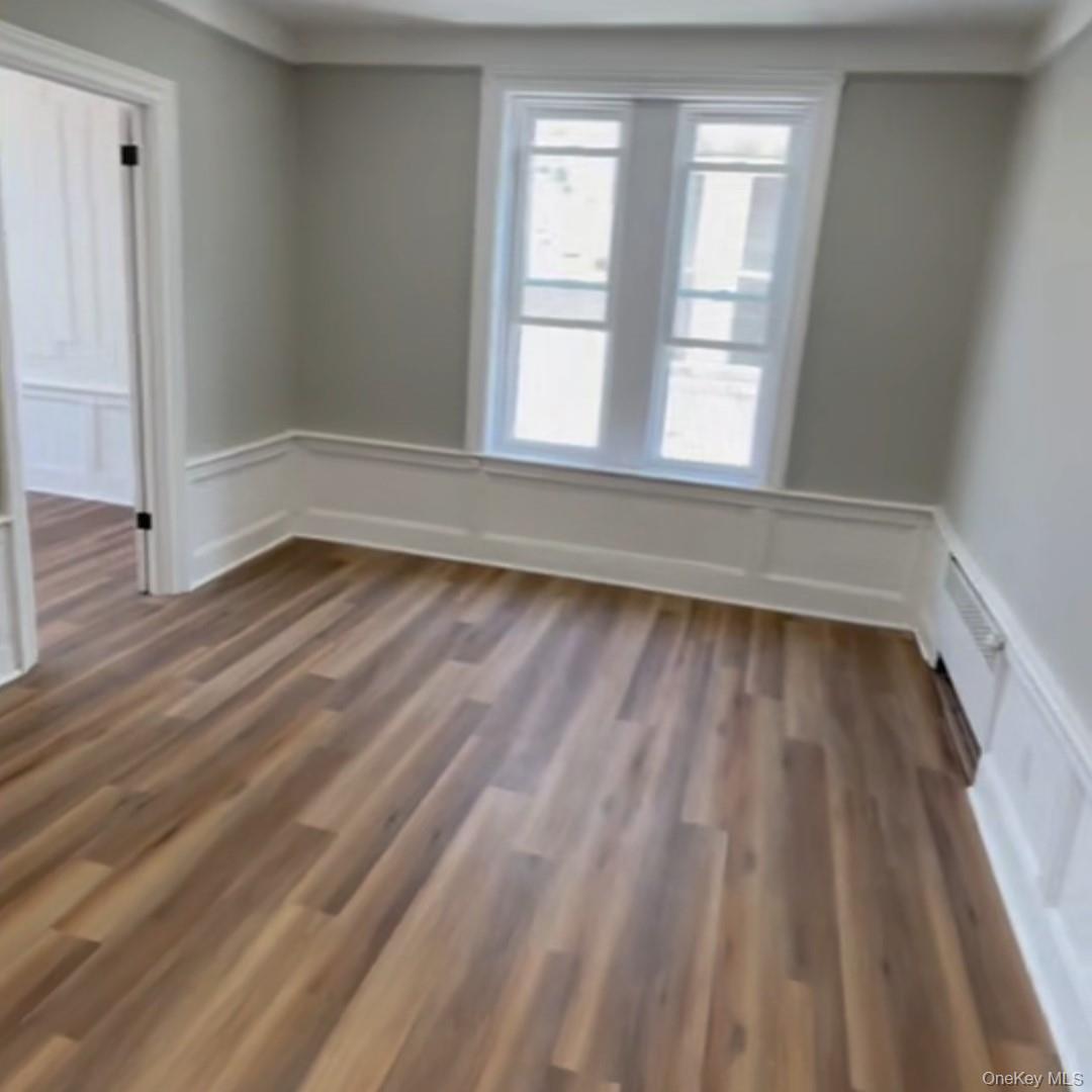 Spare room with a decorative wall, dark wood finished floors, and wainscoting