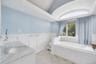 Bathroom featuring a spacious built-in soaking tub, an arched transom window, a single vanity with a stone countertop and undermount sink, wainscoting